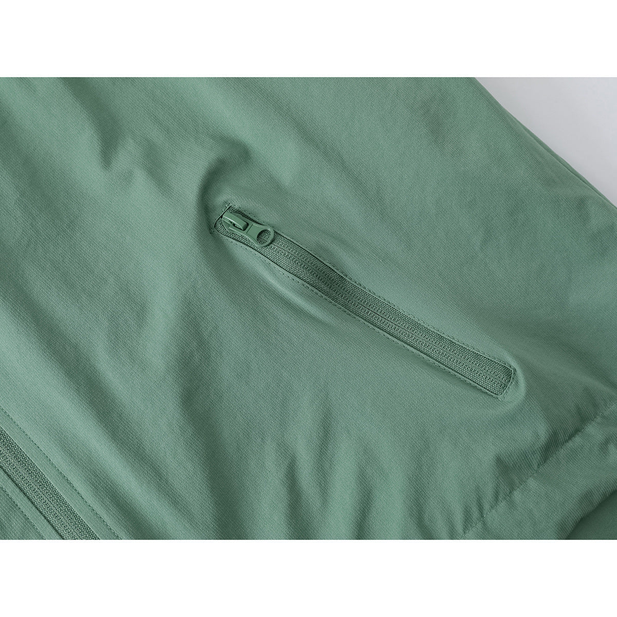 Close-up of a sage-green jacket’s angled zip pocket and surrounding seams.