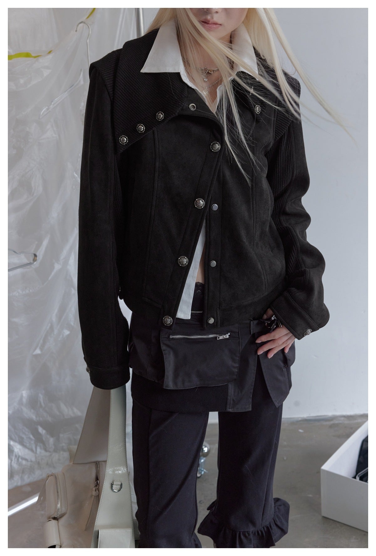 Close view of a model wearing a black jacket with an asymmetric button front, pointed lapels, and ribbed sleeves.