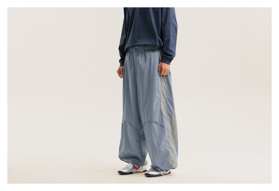 Angled side view of slate-blue oversized pants with a pale contrasting side panel and gathered cuffs on a model.