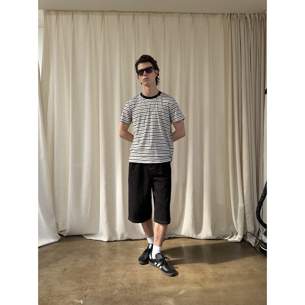 Full-length view of a model wearing a white T-shirt with thin black stripes and black shorts.
