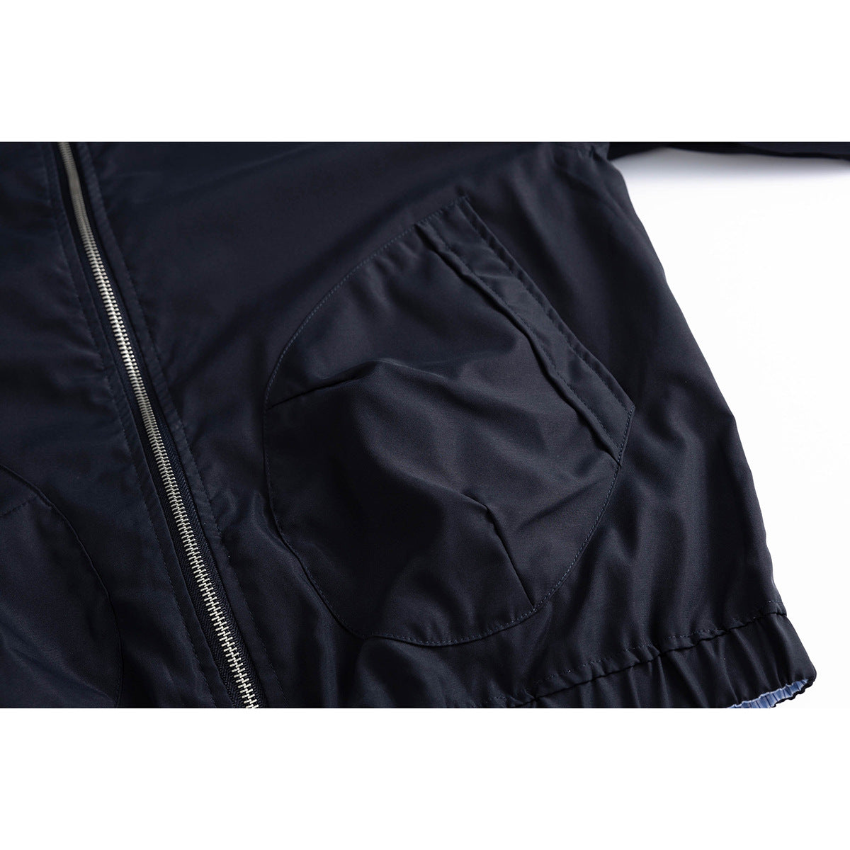 Close-up of a navy jacket’s angled front pocket, zipper, and gathered hem.