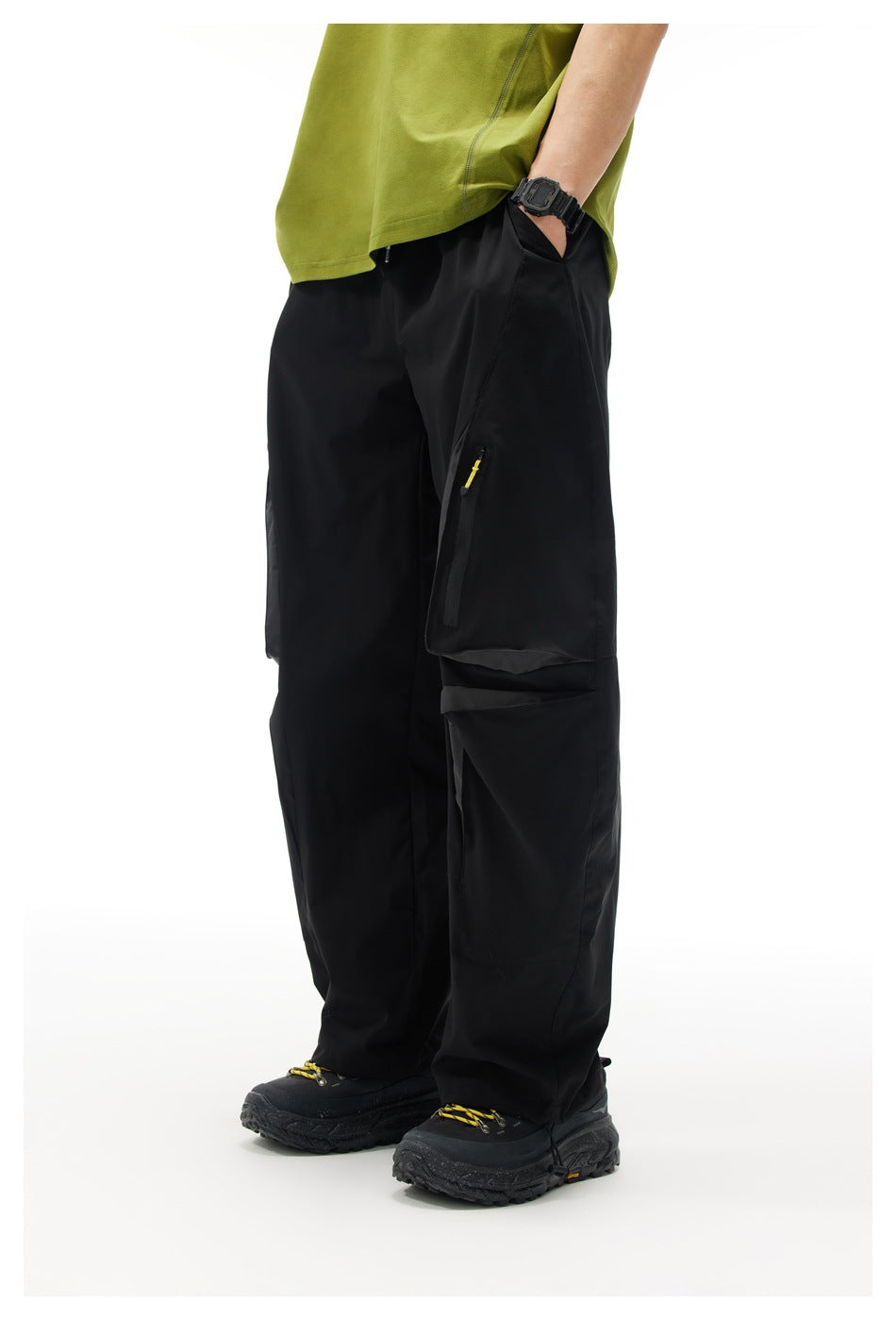 Model wearing black loose cargo pants with hand in pocket, zip pocket with yellow pull and flap pocket, front three-quarter