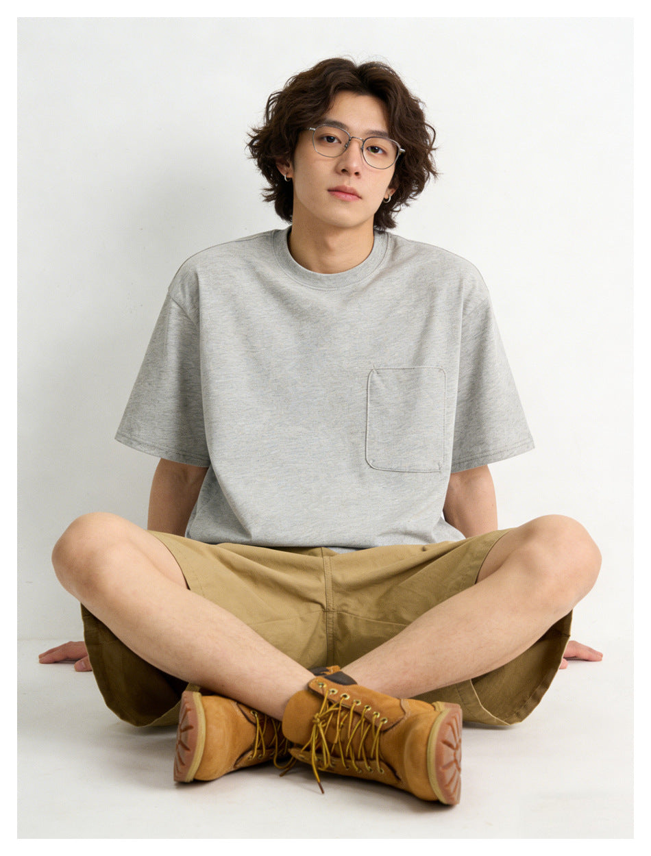 Seated model in a light gray crew-neck T-shirt with a chest pocket, shown with tan shorts.