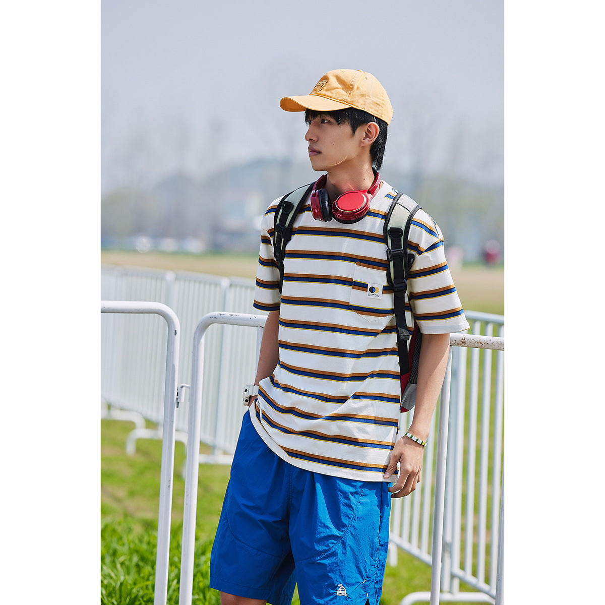 Man wearing a white striped pocket T-shirt and bright blue shorts, shown from the front outdoors.