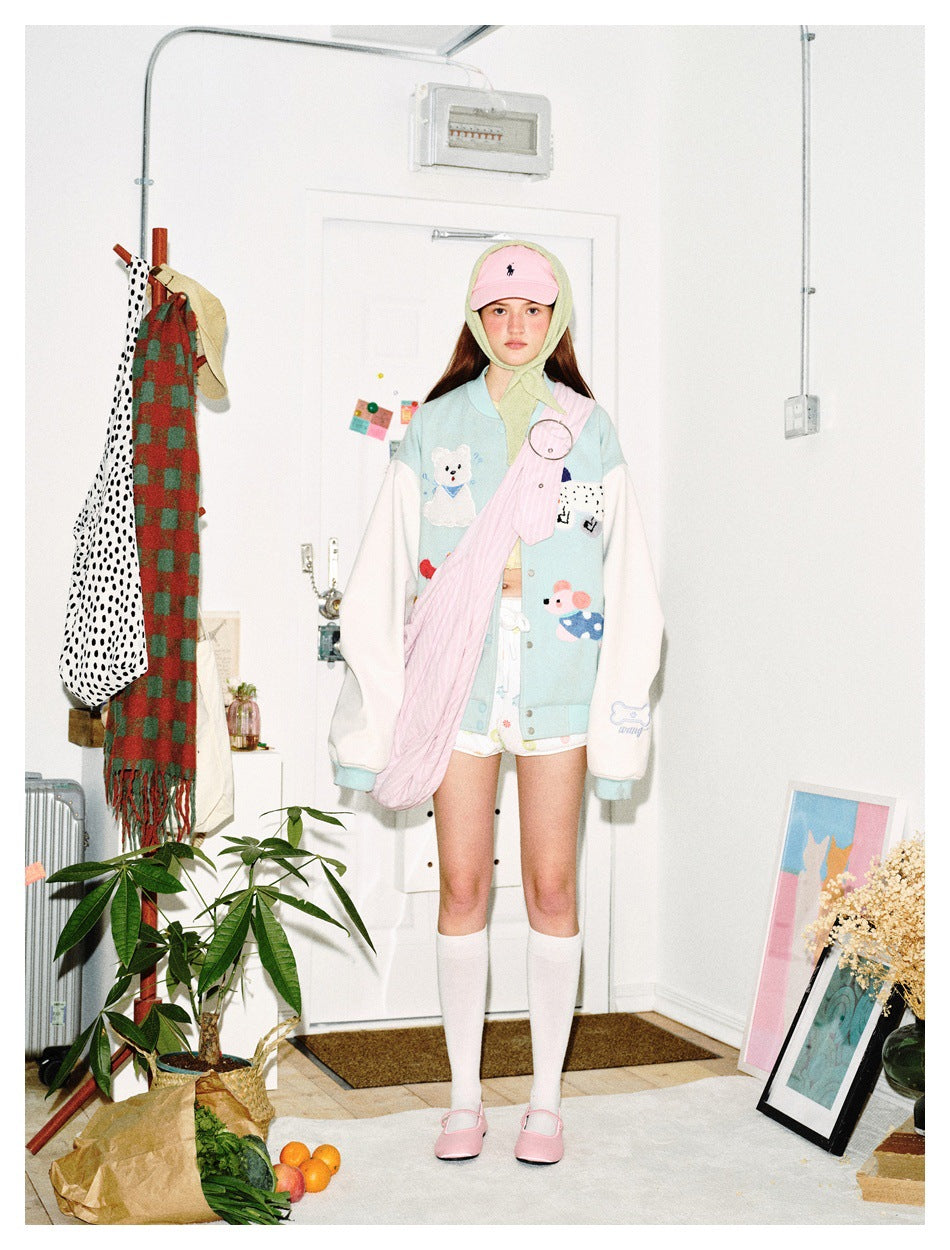 Front view of a model wearing a pale aqua jacket with white sleeves, cartoon appliqués, and a button front.