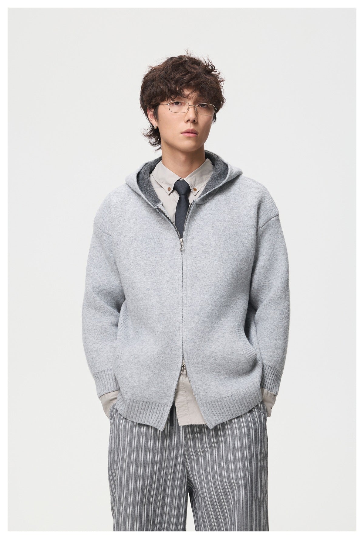 Model wearing the light gray knit zip hooded jacket unzipped over a beige shirt and tie, with the hood down