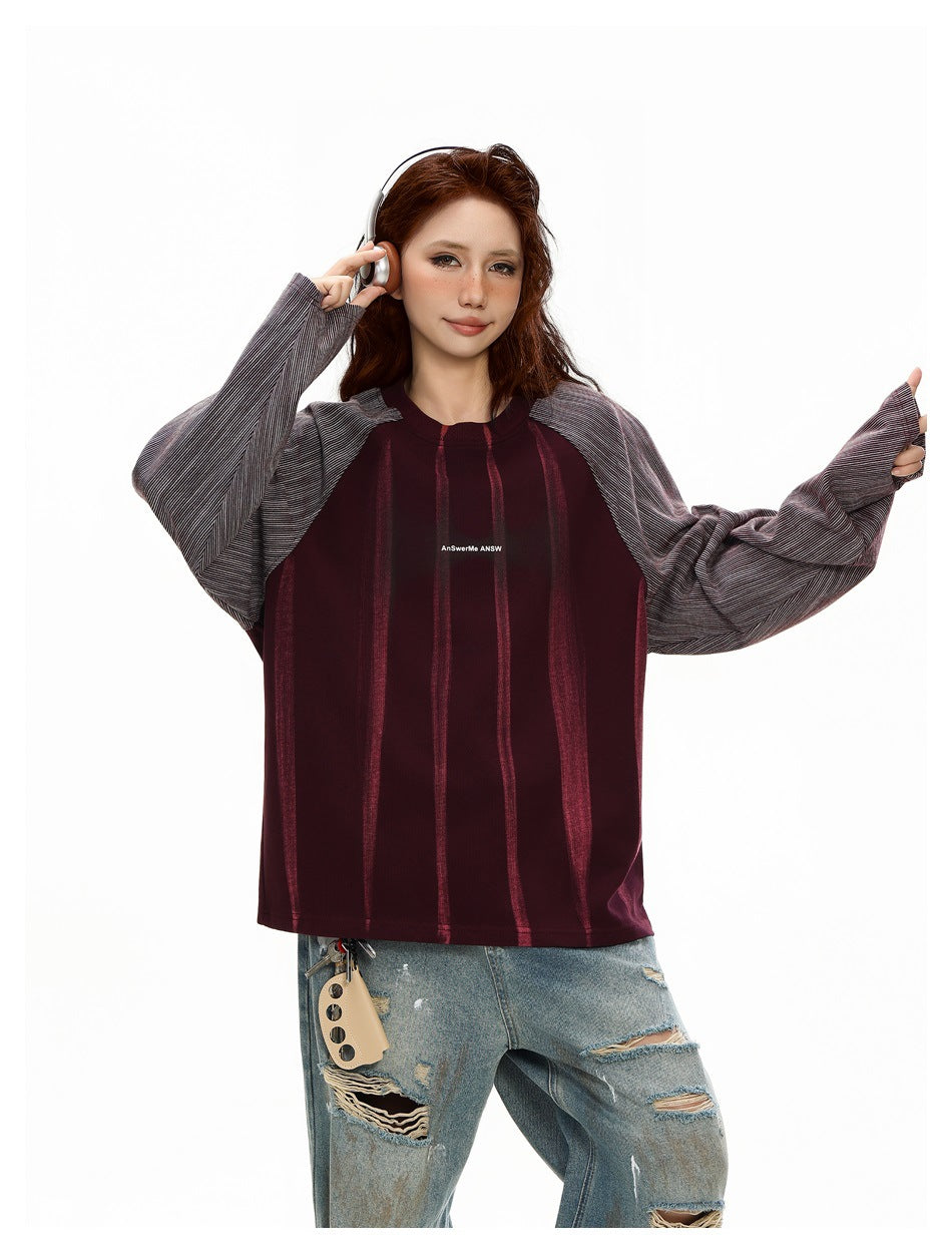Model wearing a burgundy vertically striped top with gray pinstriped raglan sleeves, paired with ripped jeans.