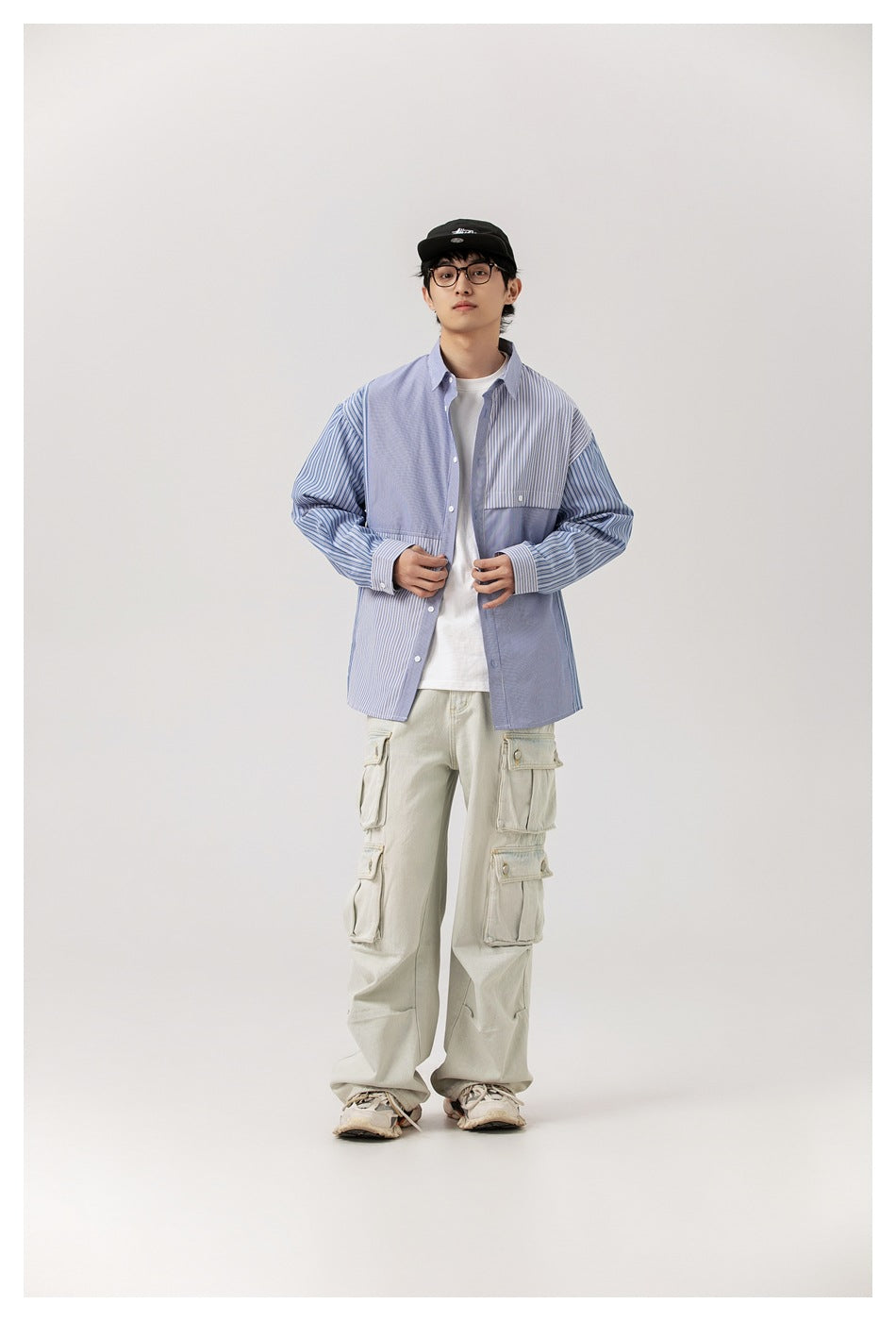 Front view of a model wearing an open blue patchwork striped shirt over a white tee with pale cargo pants.