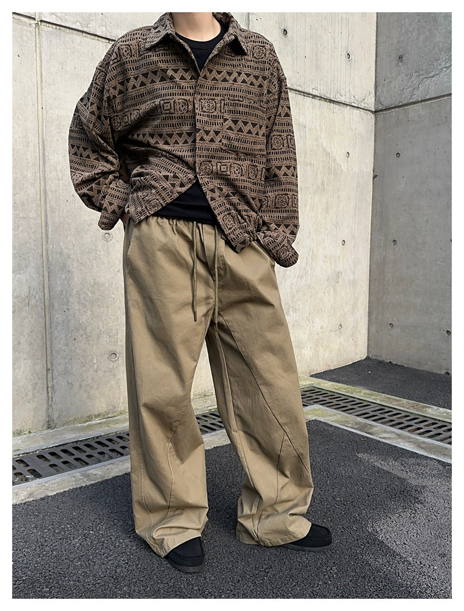 Angled view of a model wearing taupe wide-leg drawstring pants and a geometric-patterned brown shirt.