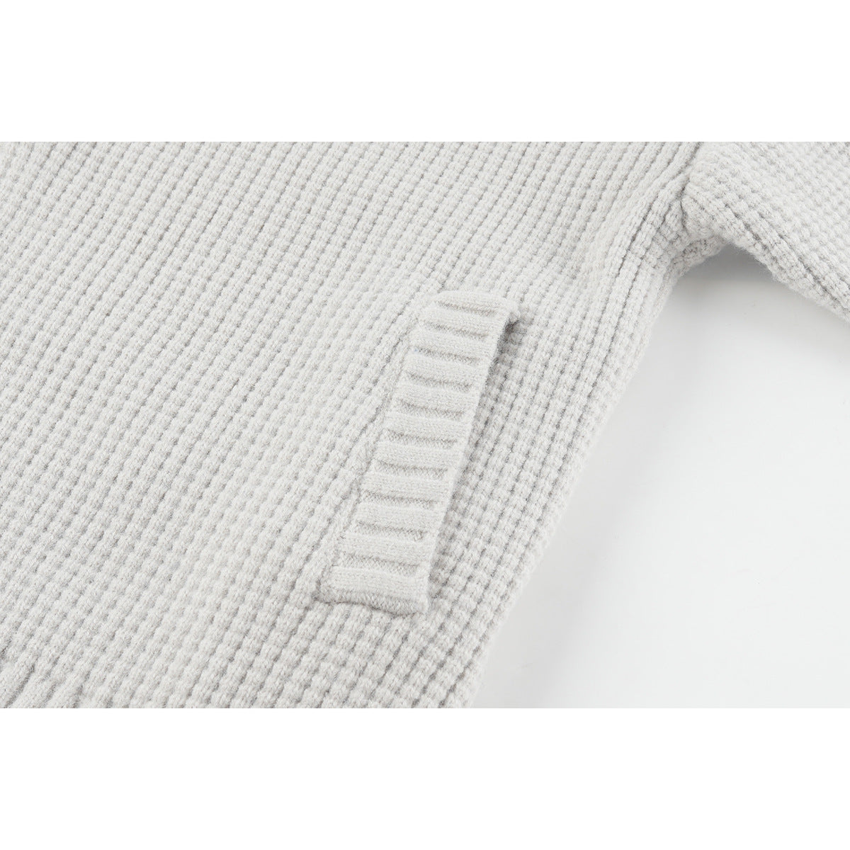 Close-up of a light gray textured knit cardigan's narrow vertical welt pocket.