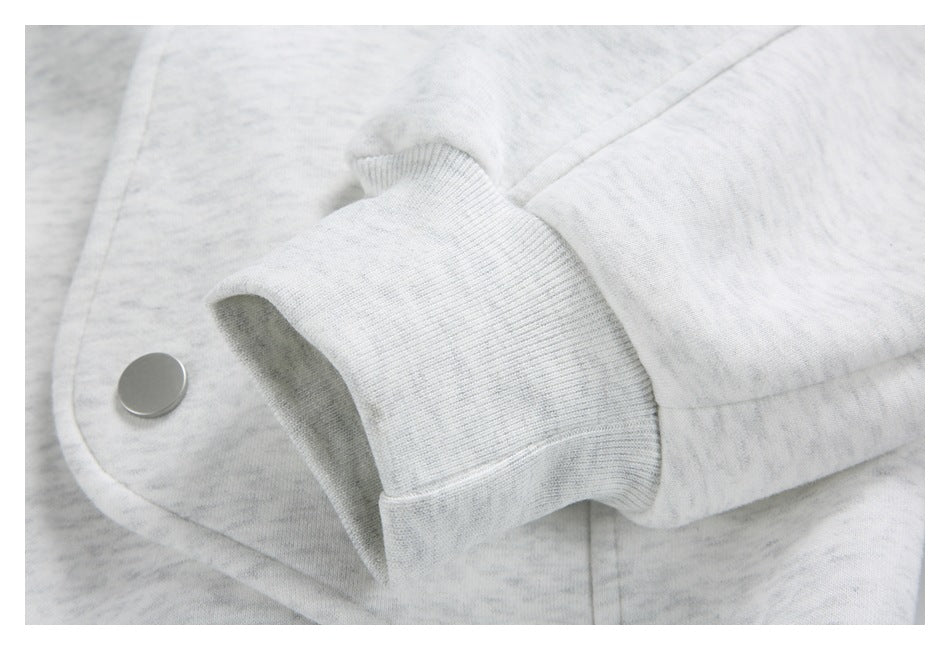 Close-up of a light gray marled garment cuff beside a round metal snap button.