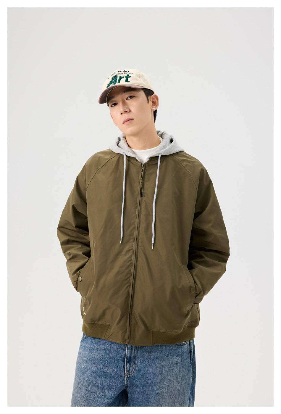 Model wearing an olive zip-front jacket with gray hood, ribbed cuffs and hem, layered over jeans.