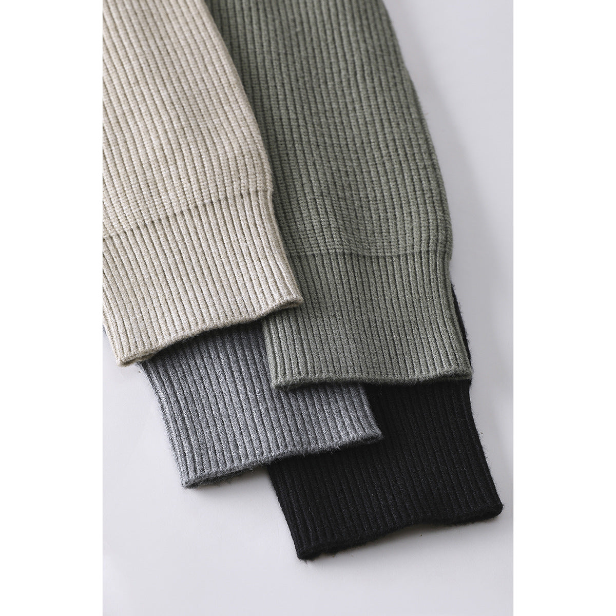 Close-up of ribbed cuffs from cream, sage, gray, and black knit cardigans.
