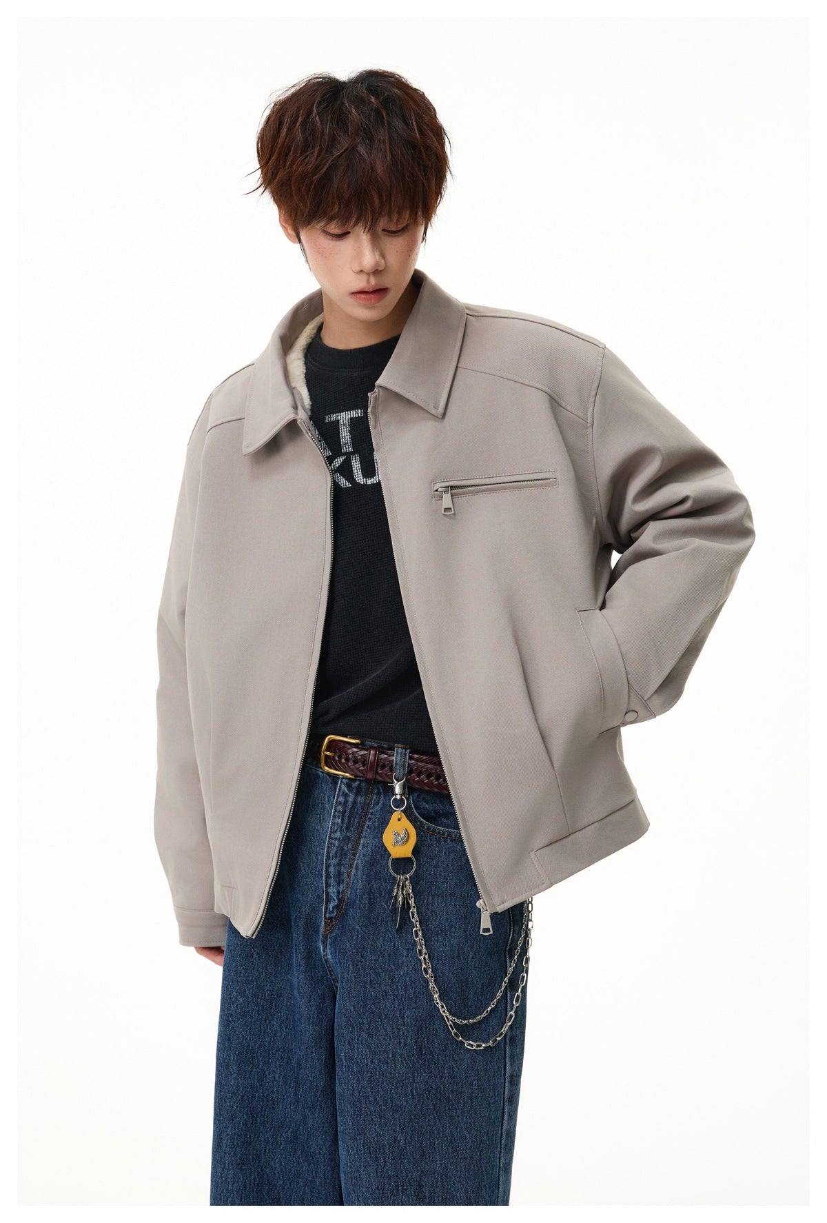 Model wearing a light taupe zip jacket with a pointed collar and chest zip pocket, styled with dark jeans.