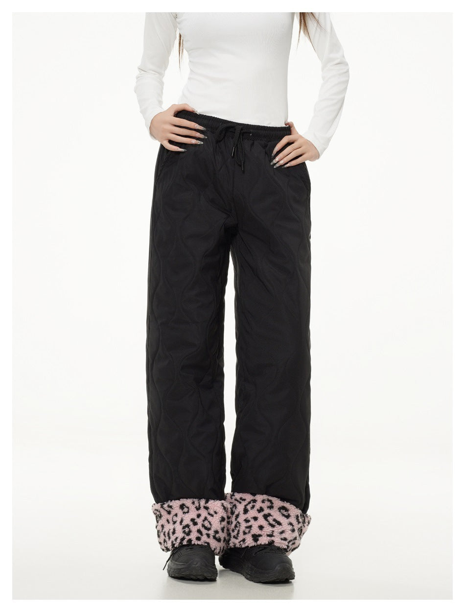 Front view of a model wearing black quilted wide-leg pants with a drawstring waist and pink leopard-print ankle cuffs.