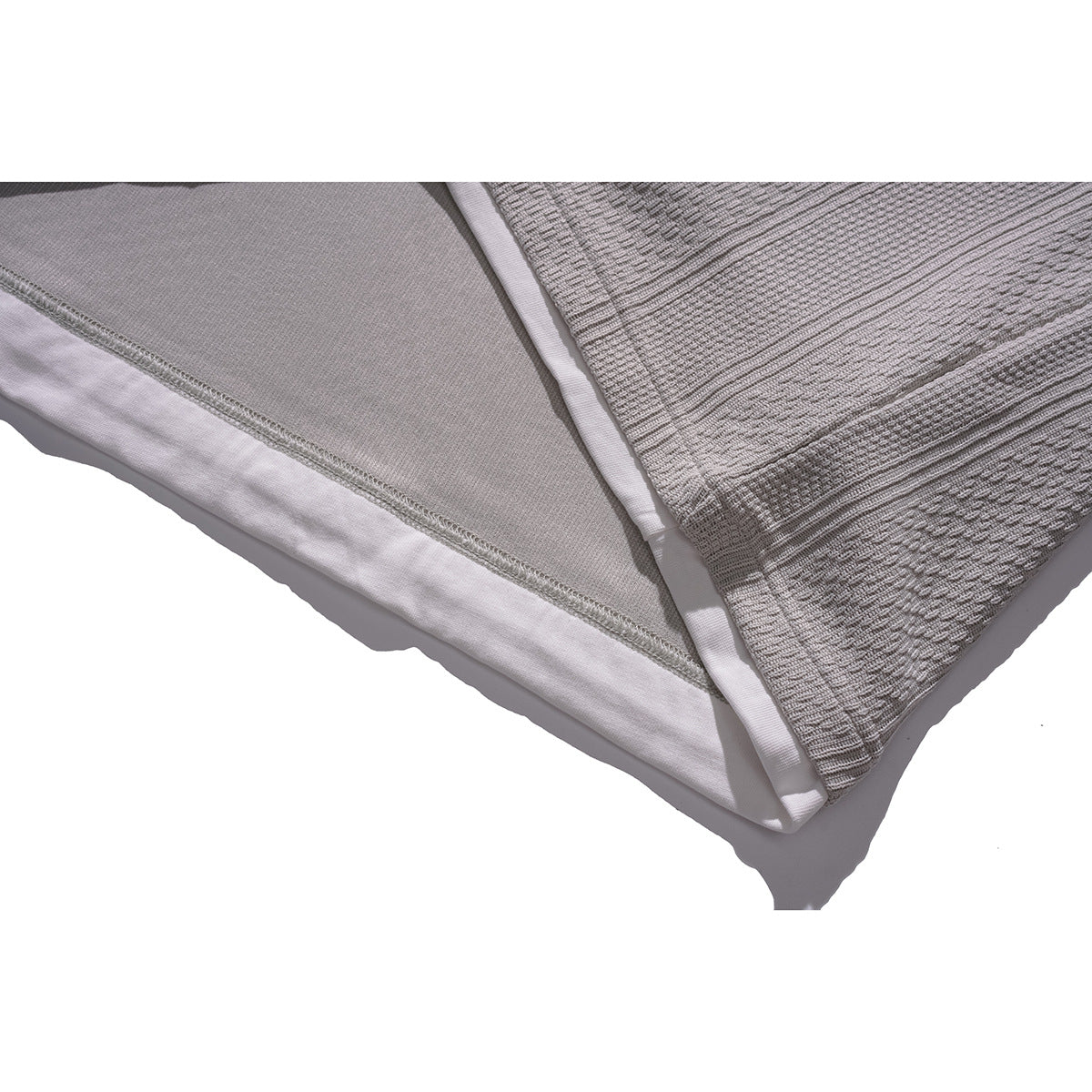 Close-up of the layered hem of a light gray textured top, showing the inner white layer and stitching.