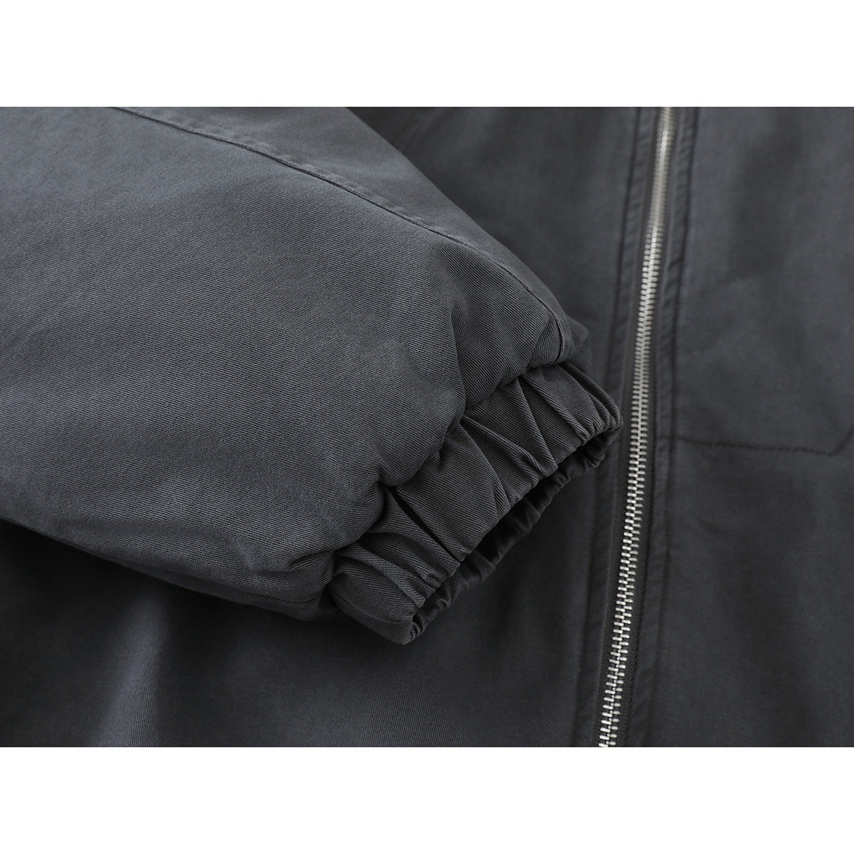 Close-up of a charcoal jacket sleeve with a gathered elastic cuff beside the front zipper.