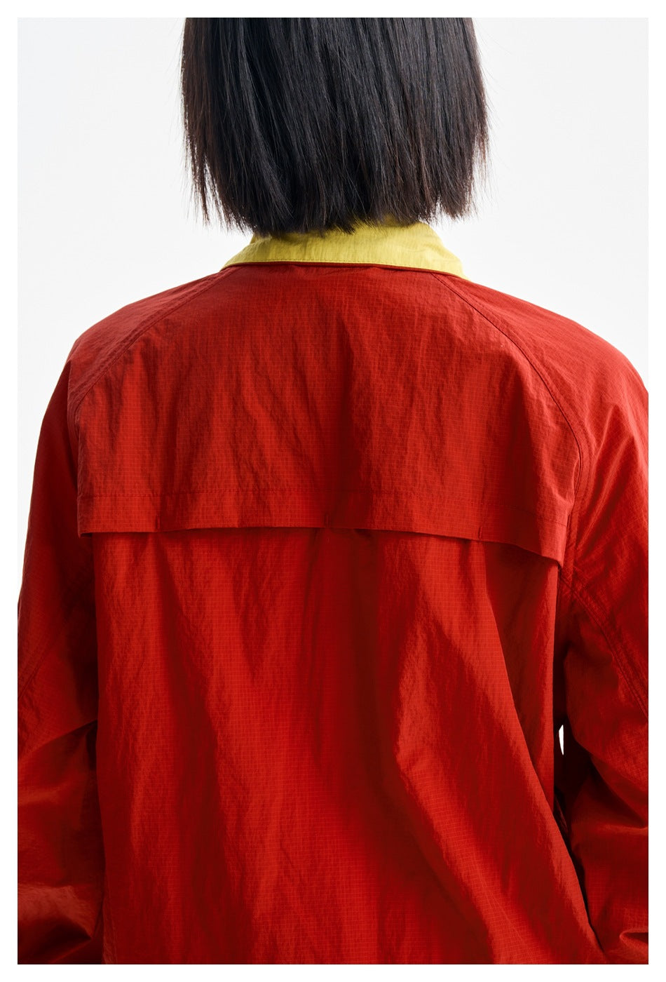 Close-up rear view of a red jacket showing its yellow collar and horizontal back yoke panel.