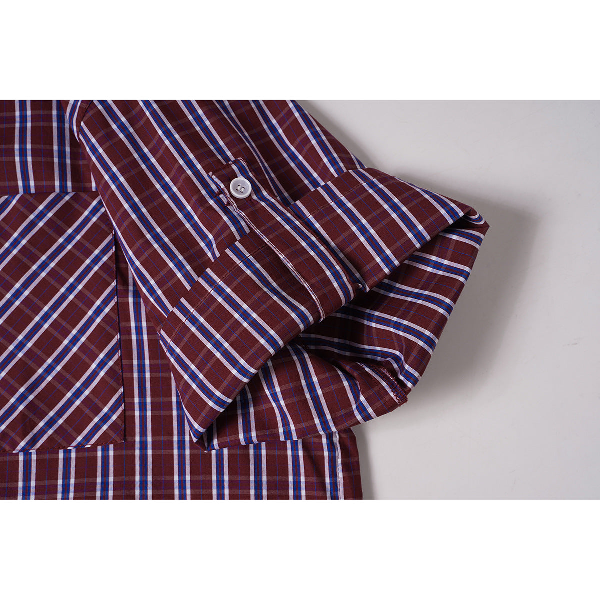 Close-up of a rolled sleeve and button tab on a burgundy plaid shirt.