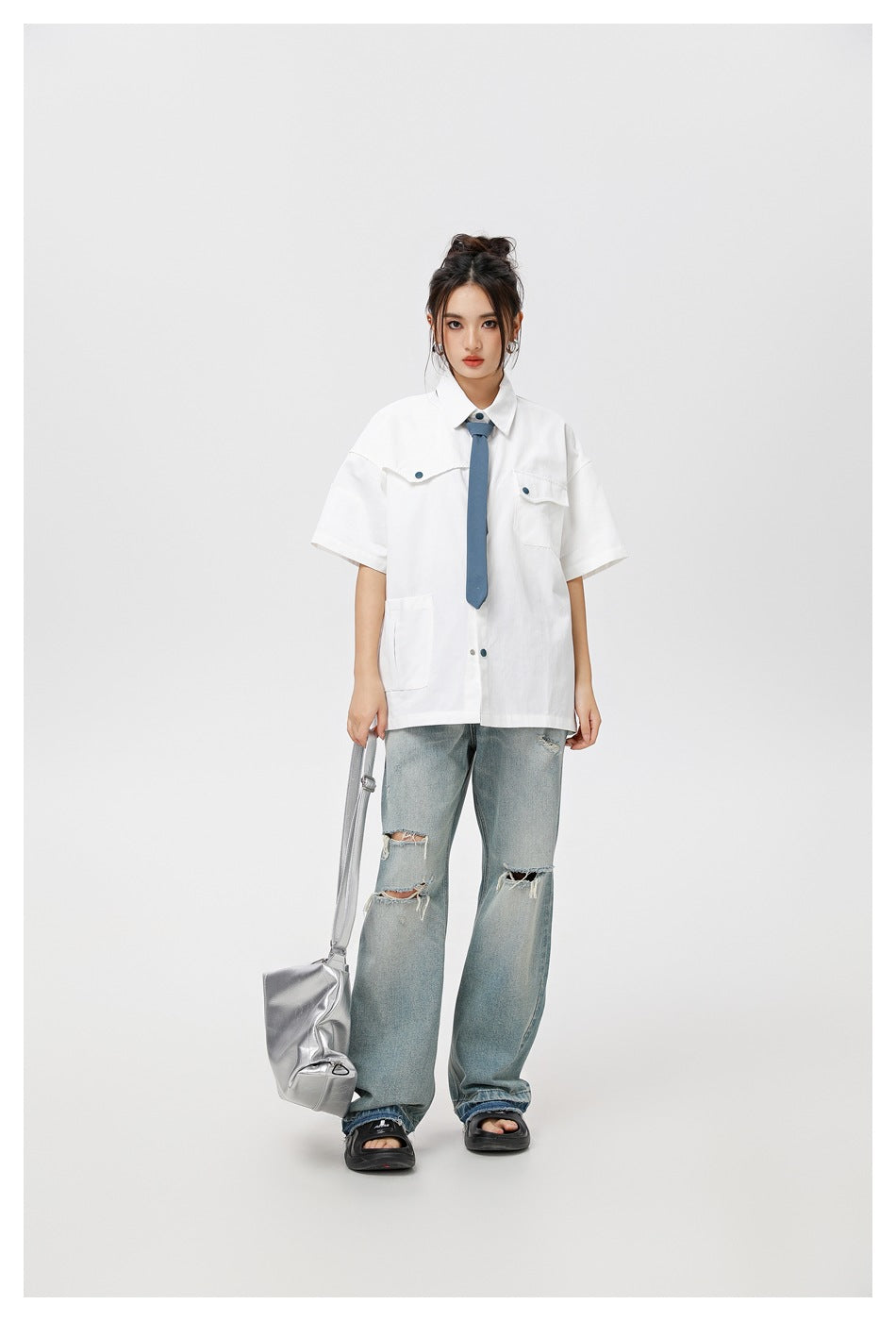 Front view of a model in a white short-sleeve shirt with a blue tie and ripped jeans.