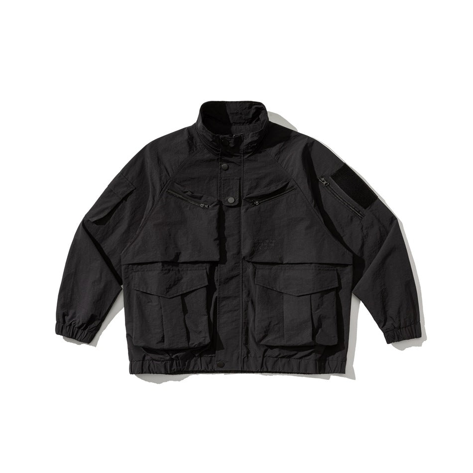 Black stand-collar utility jacket flat lay with large flap pockets, zip chest pockets and elastic cuffs