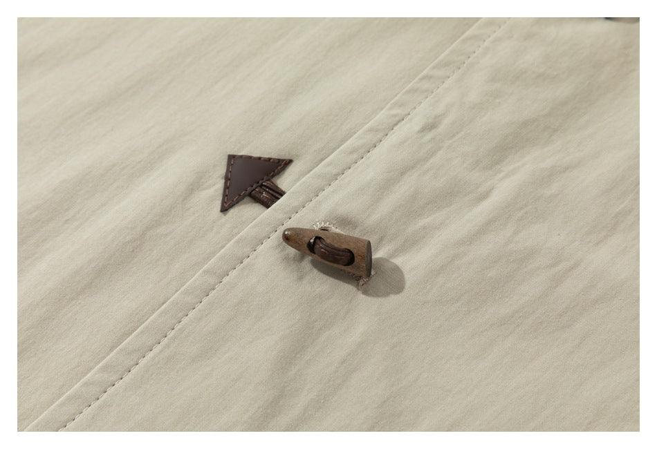 Close-up of a beige garment with a brown wooden toggle fastener and triangular leather-like patch.