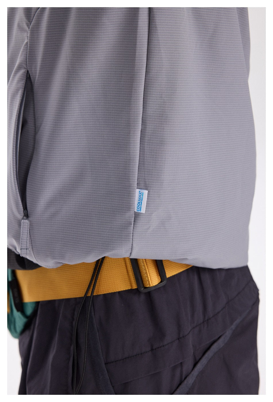 Close-up of a gray vest showing fine horizontal texture, a zip pocket, and a small Coolmax fabric tag.