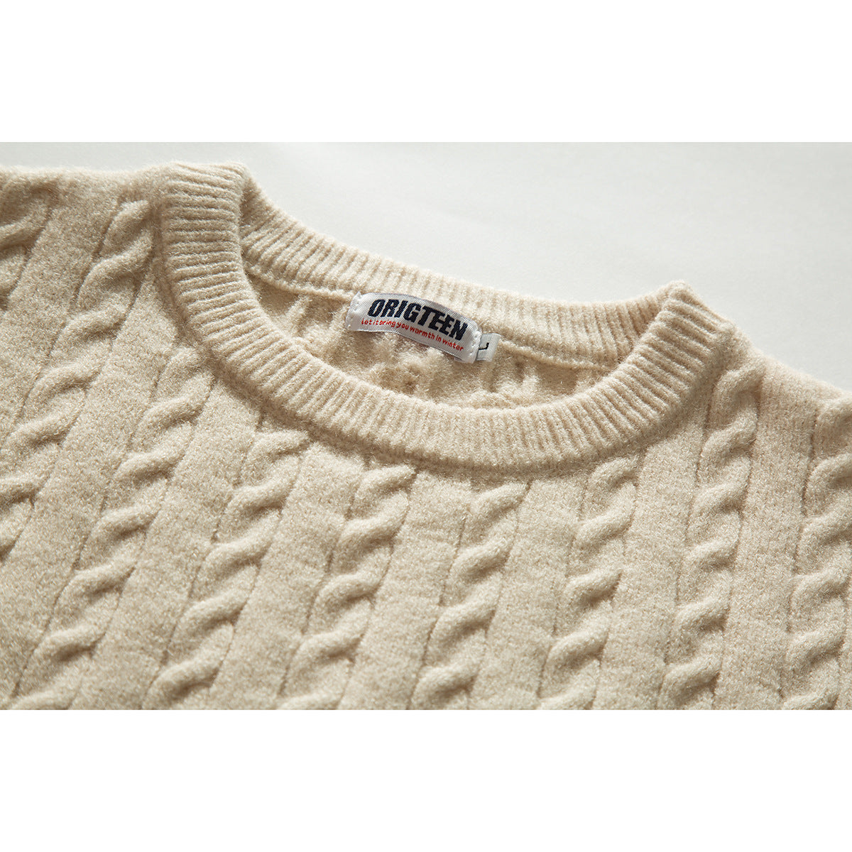 Close-up of an ivory cable-knit sweater showing its ribbed crew neck and sewn-in neck label.