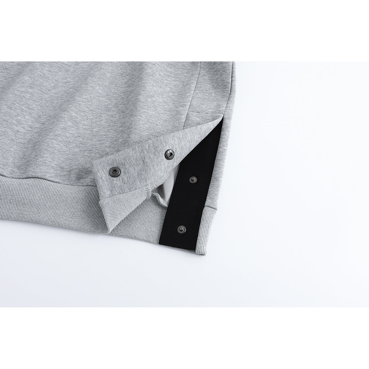 Close-up of a heather-gray sweatshirt's ribbed hem and side opening, fastened with metal snaps over a black panel.