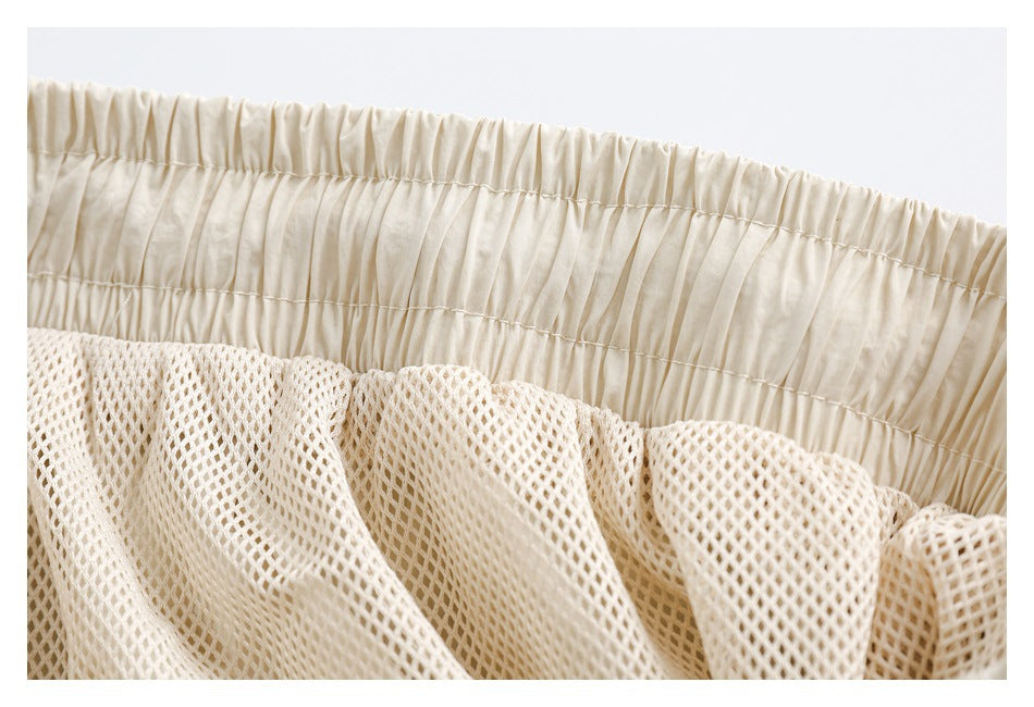 Close-up of a gathered elastic waistband above cream open-mesh fabric.