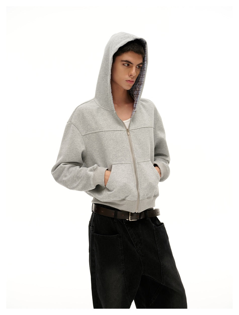 Model wearing a light gray zip-up hoodie with plaid hood lining and black pants, hands in the pockets.