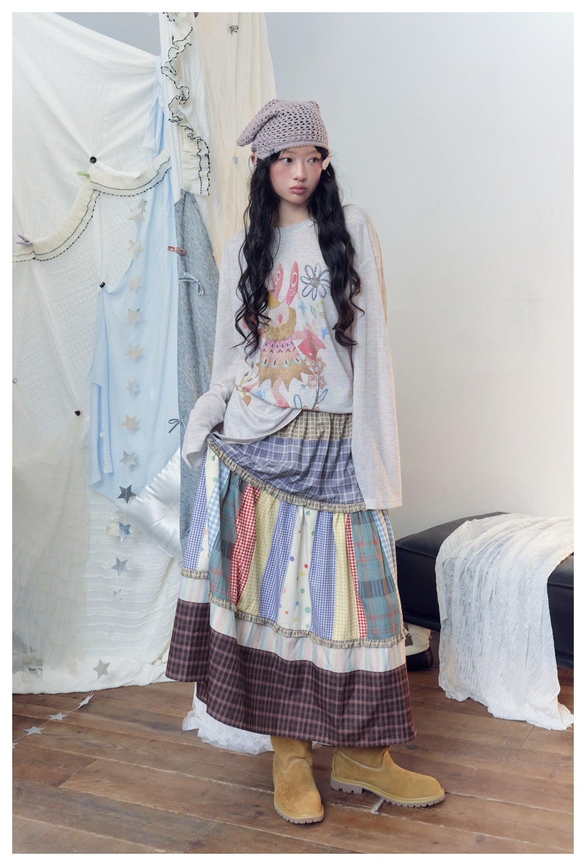 Model lifts the skirt to show its gathered plaid waist and colorful patchwork tiers.