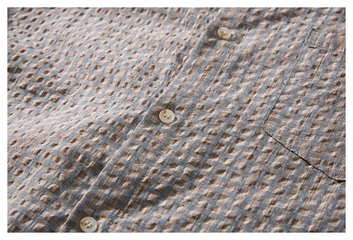Close-up of a gray-brown patterned shirt front with light buttons, a placket, and part of a patch pocket.