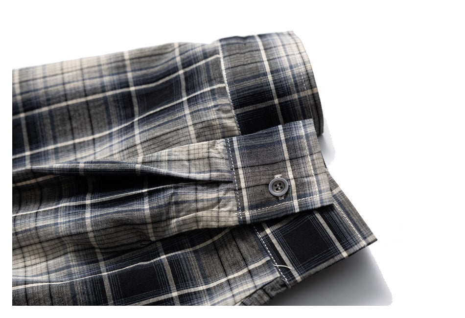 Close-up of the buttoned cuff and folded sleeve of a black, gray, and cream plaid shirt.