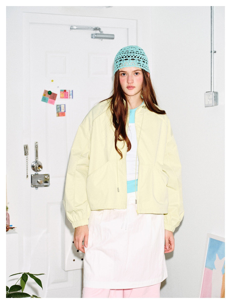 Model wearing light yellow cropped zip jacket over a white skirt with a light blue crochet hat