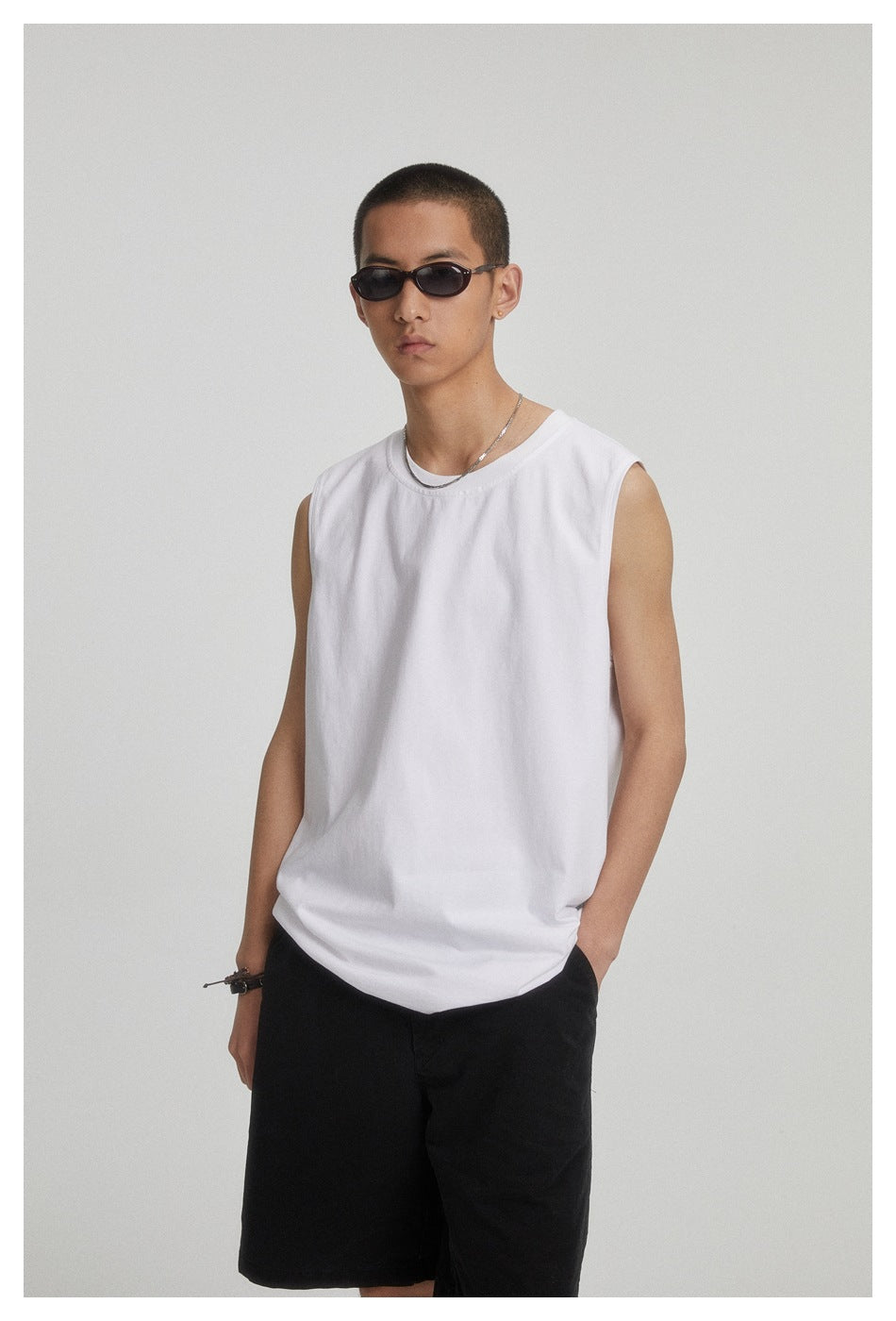 Model wearing a plain white sleeveless crew-neck shirt with black shorts, shown from head to mid-thigh.