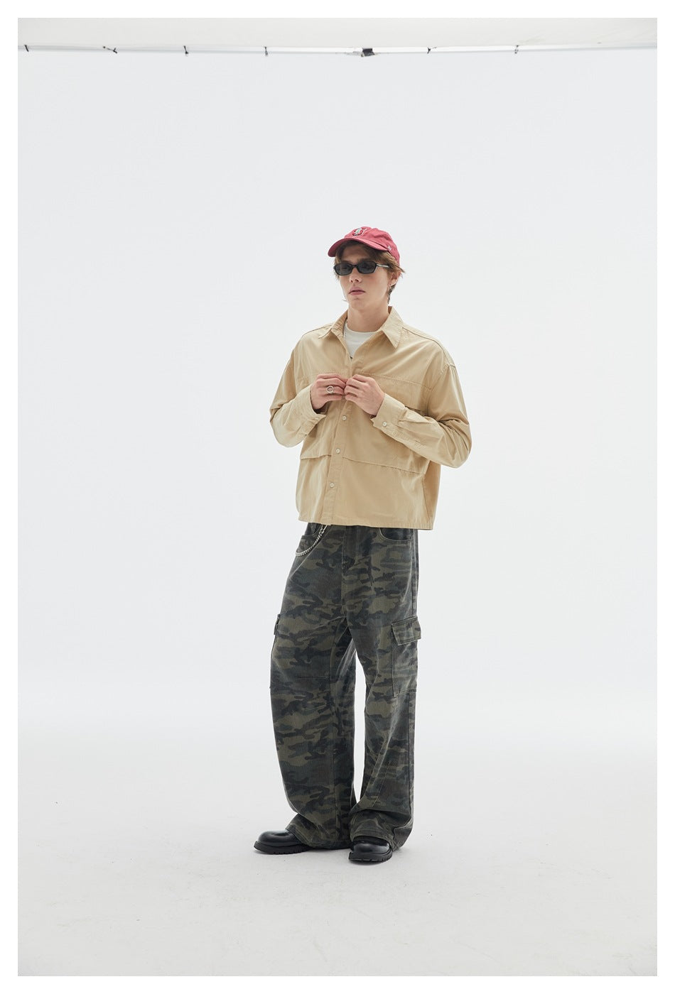 Model fastening a beige button-up overshirt over a white shirt, with loose dark camouflage cargo pants.