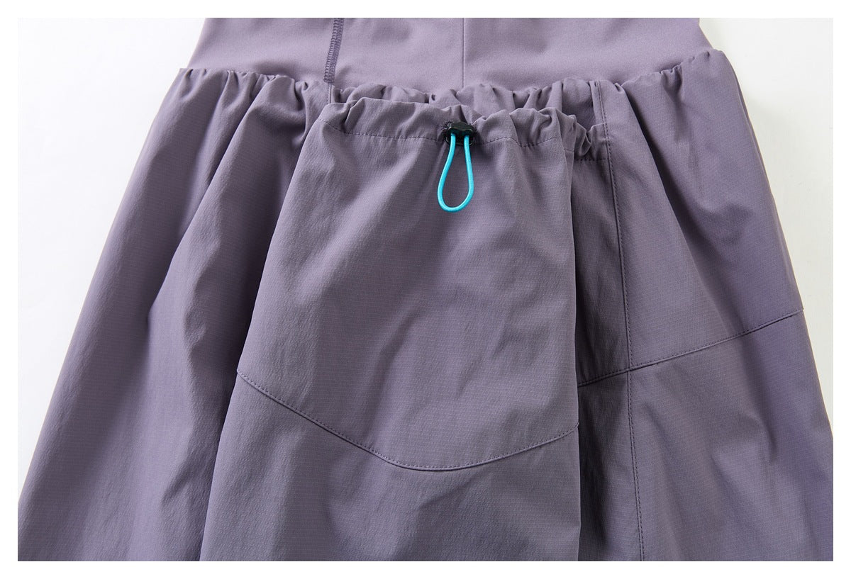 Close-up of a large skirt pocket with a turquoise loop cord and black toggle on muted purple fabric.