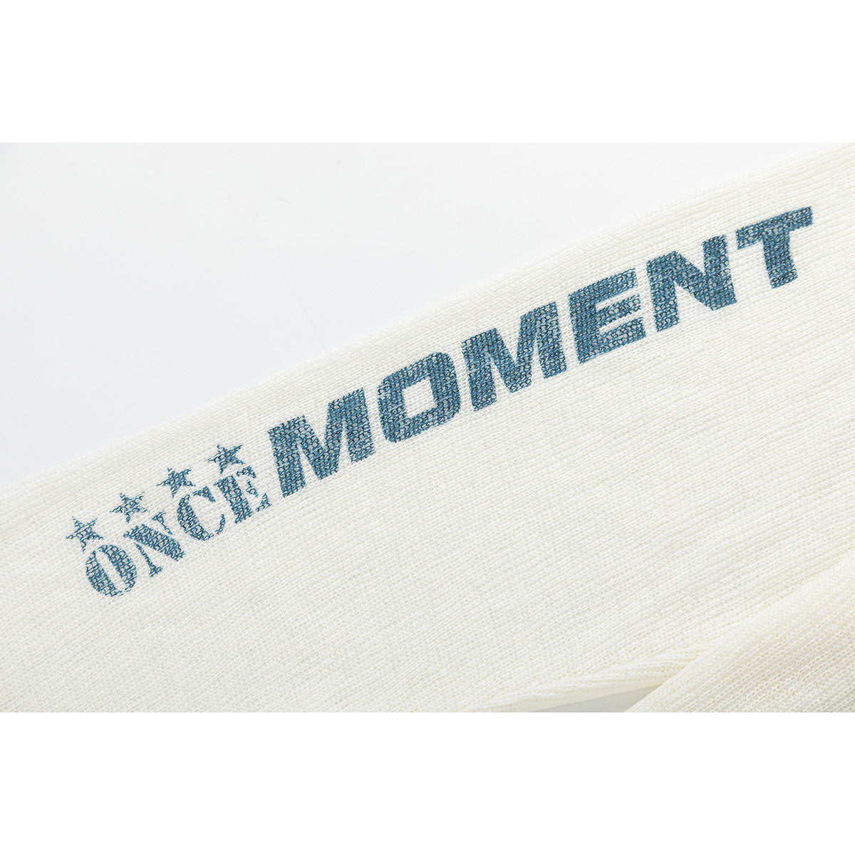 Close-up of an ivory knit sleeve with blue “ONE MOMENT” lettering and star graphics.