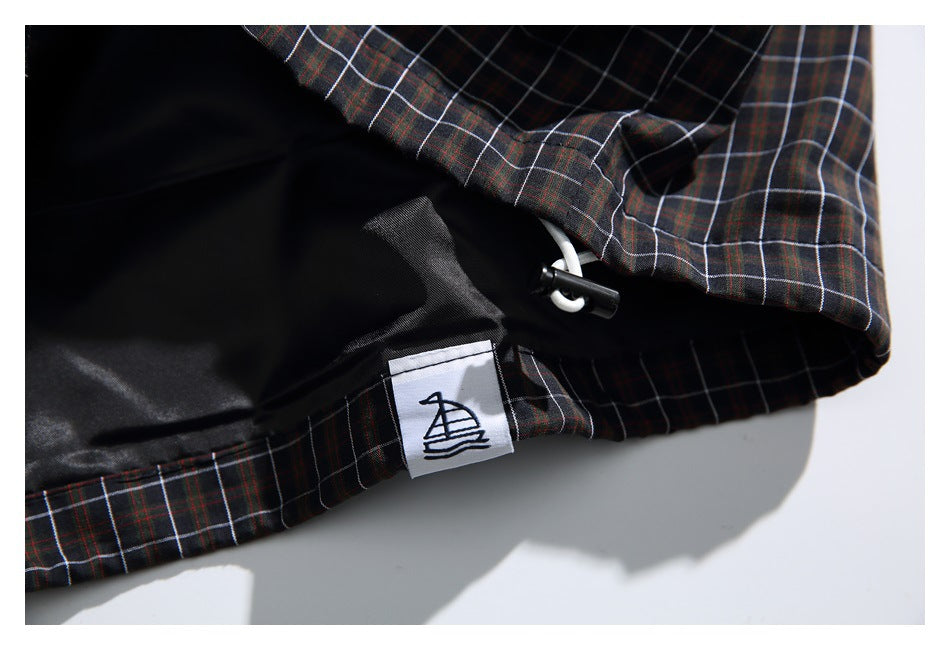 Inside detail of a dark plaid garment showing black lining, a drawcord toggle, and a small sewn emblem label.