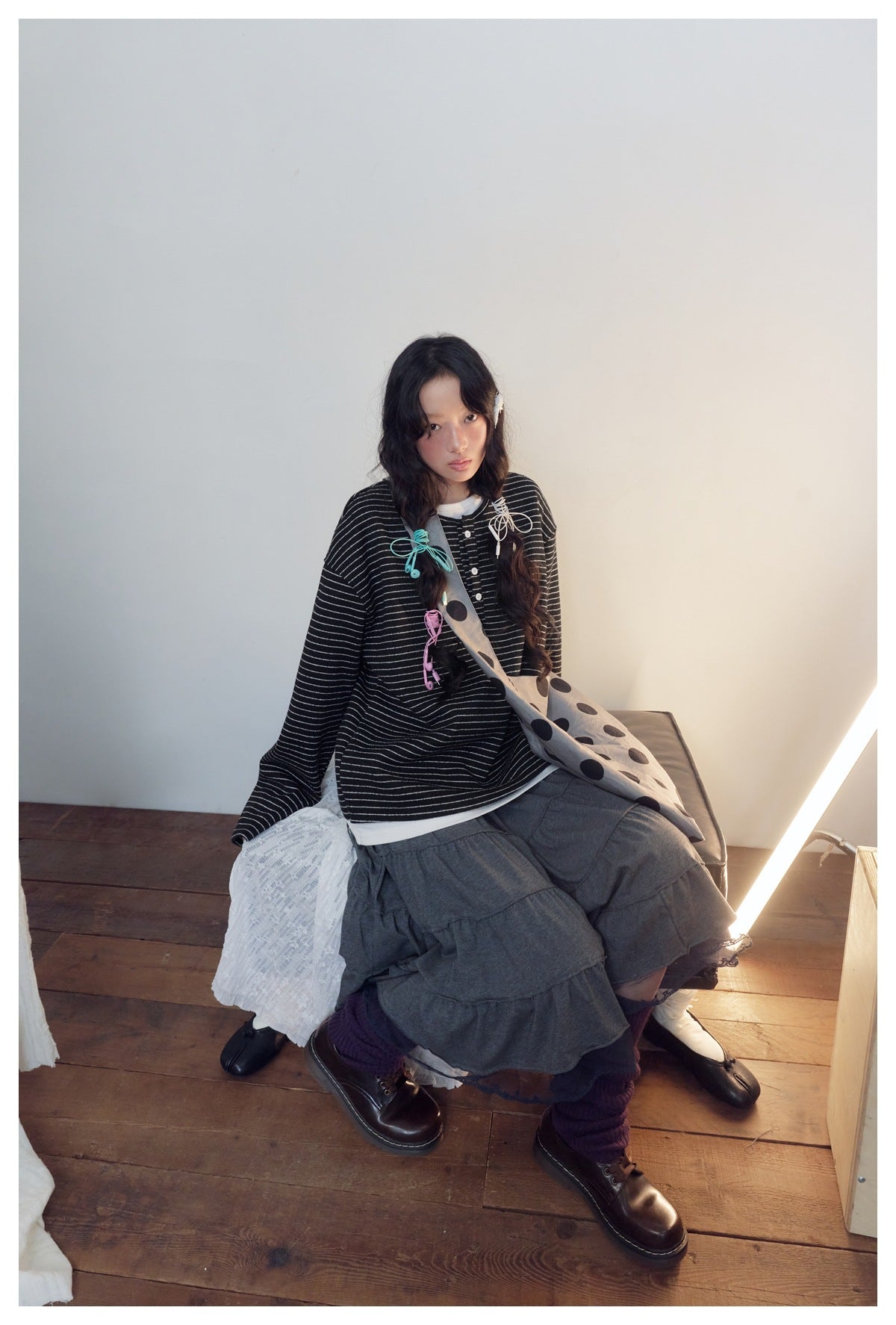 Model wearing a black long-sleeve top with thin white stripes and a short button placket, paired with a layered skirt.