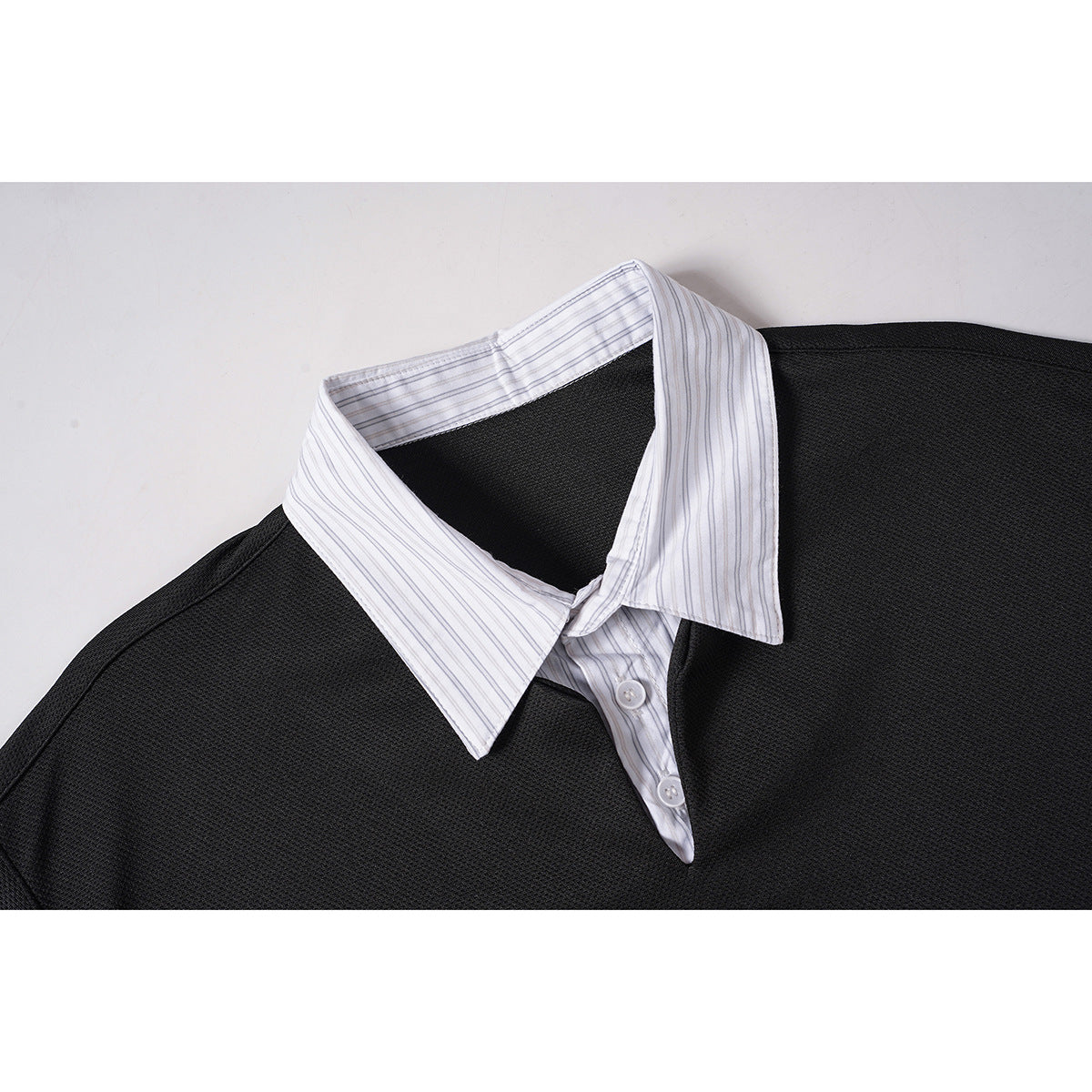 Close-up of a black textured polo with a white, fine-striped shirt collar and button placket.