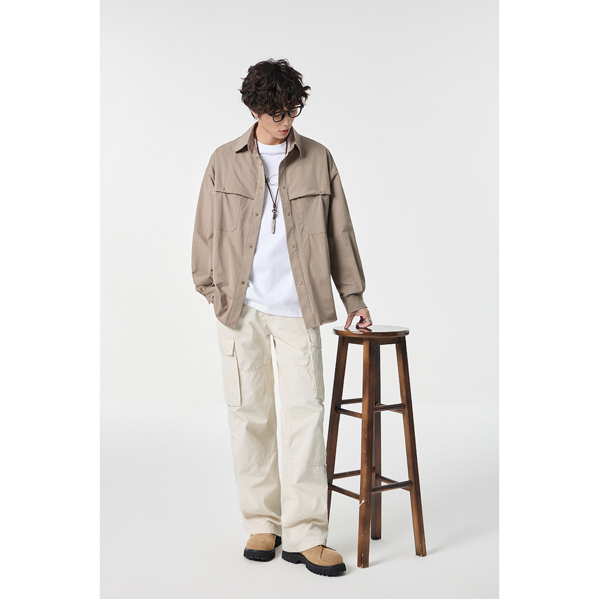 Model wearing a taupe oversized button-up shirt with flap chest pockets and cream cargo pants.