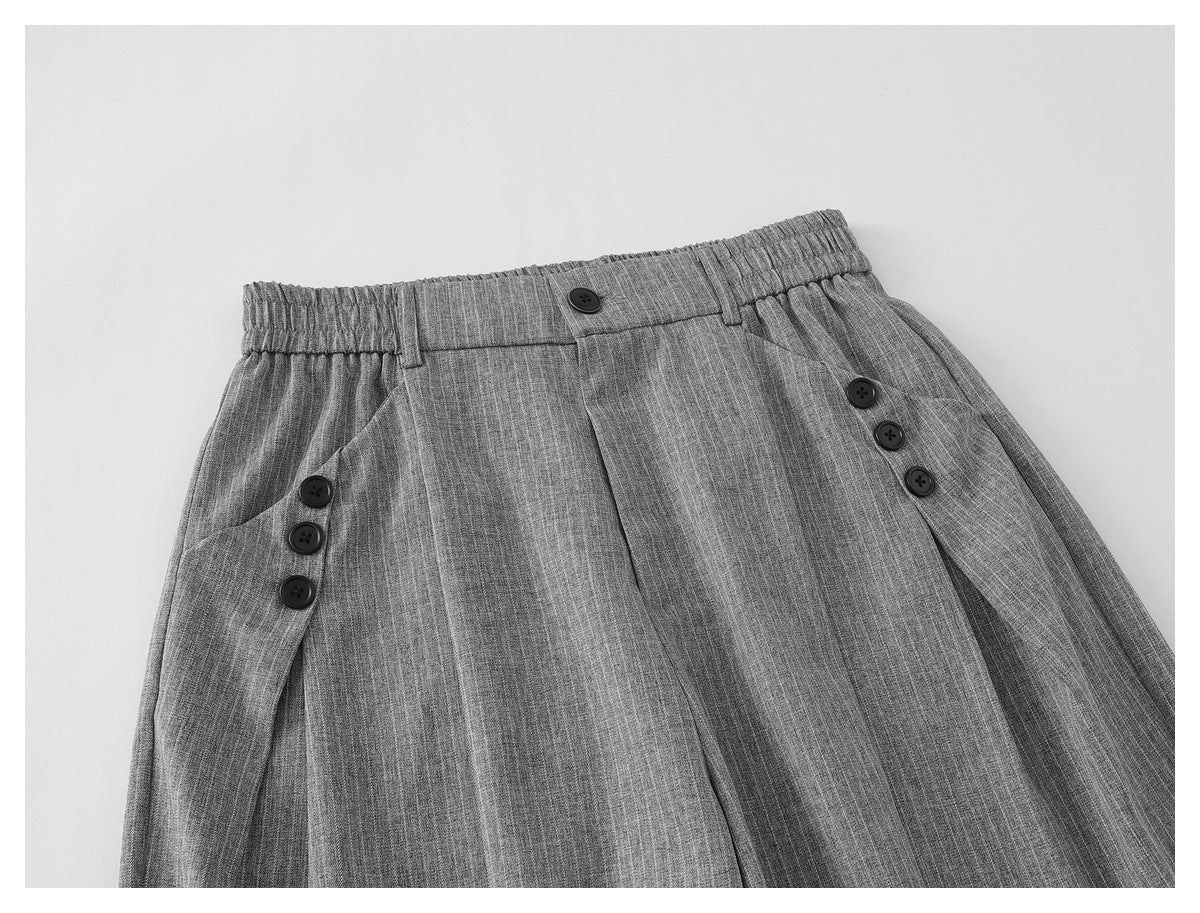 Close-up of the gray pinstripe trousers' waistband, front button, pleats, and buttoned side tabs.