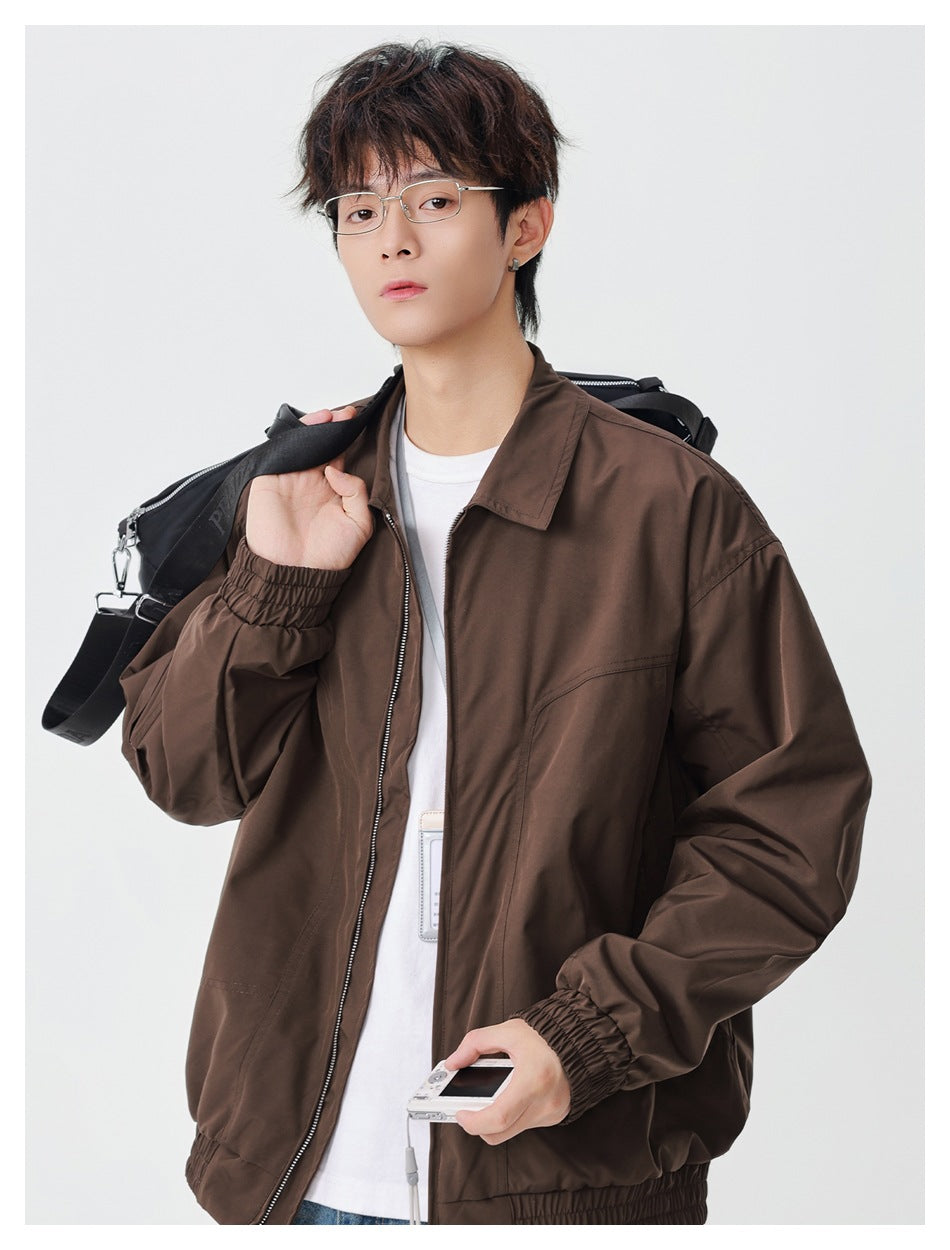Model wearing a brown collared zip jacket with elastic cuffs and hem, carrying a black shoulder bag.