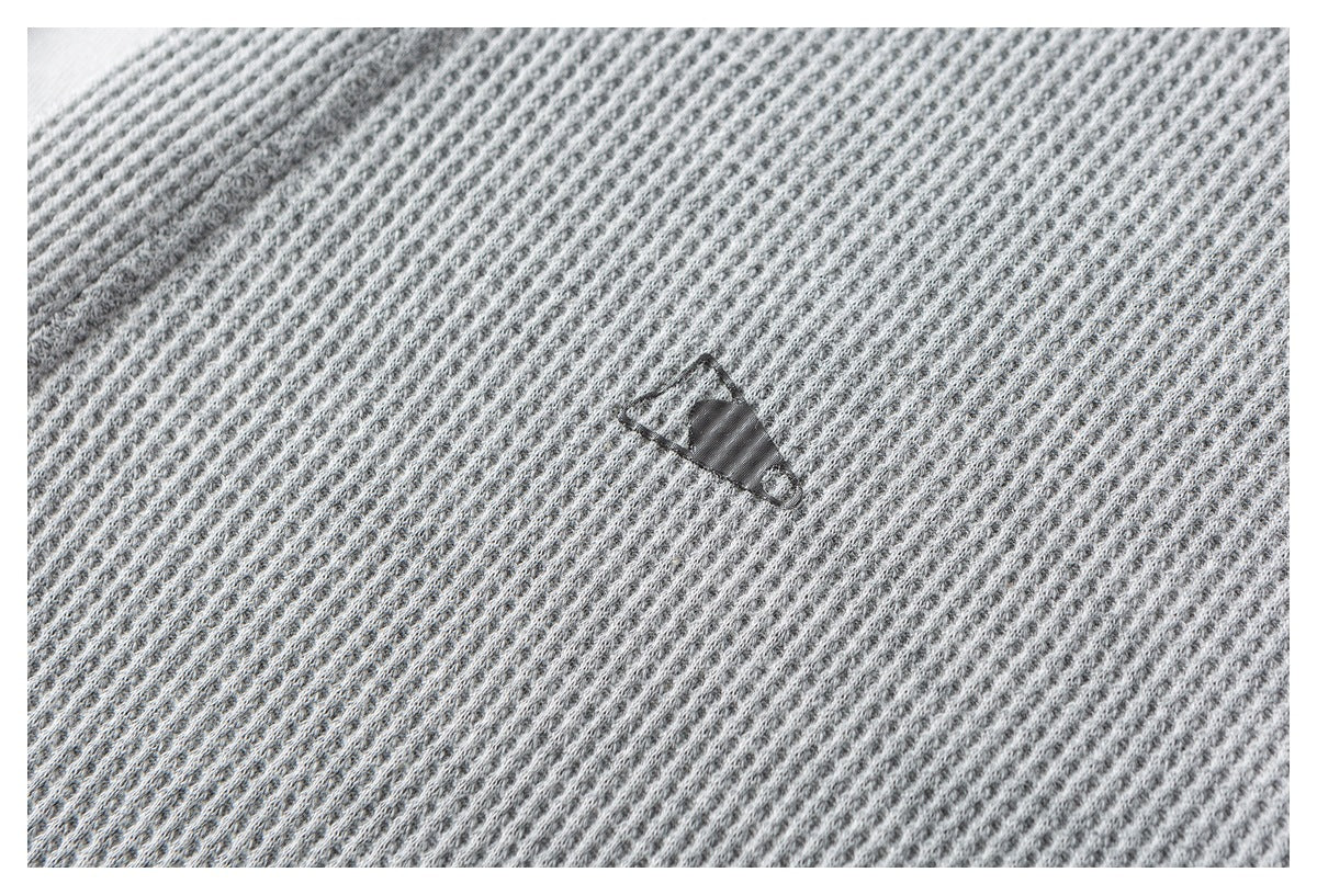 Close-up of light gray waffle-knit fabric with a small dark emblem.