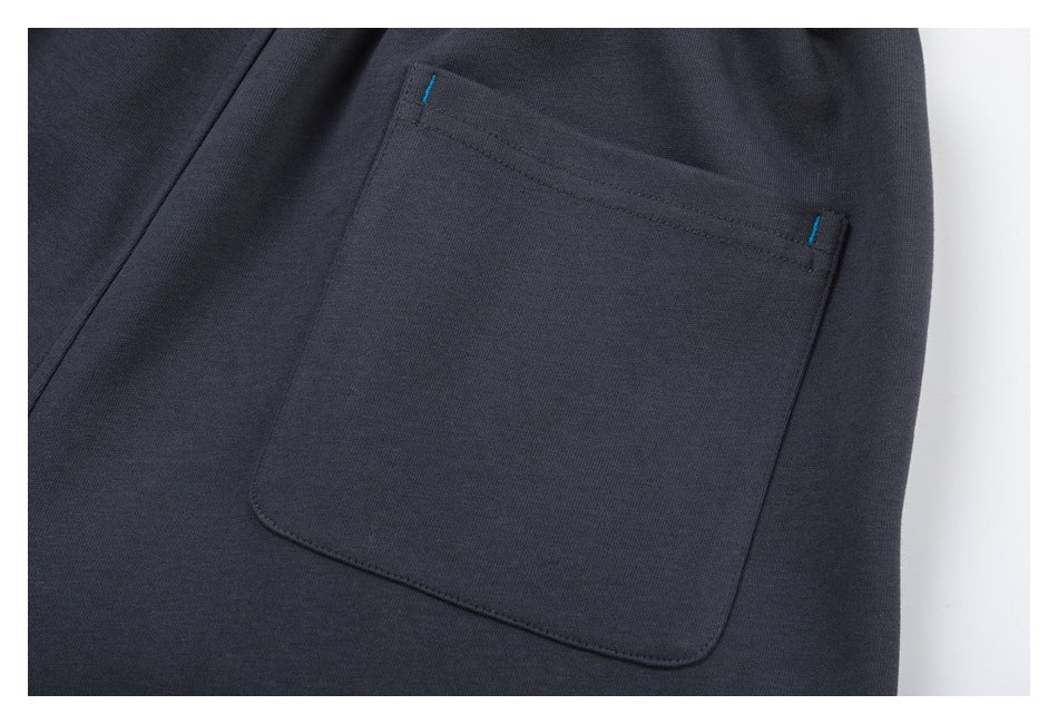 Close-up of a rectangular patch pocket with blue bar-tack stitching on charcoal pants.