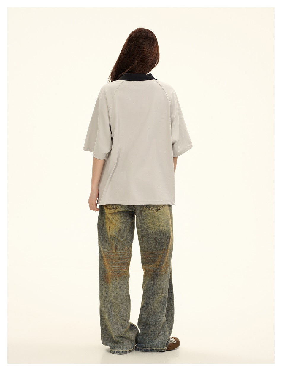 Rear view of a model wearing an oversized light gray polo with a black collar and loose, faded jeans.