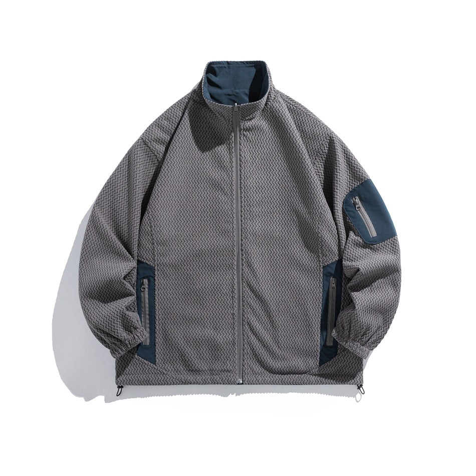 Dark gray textured zigzag-weave stand-collar zip jacket with blue contrast panels and zippered pockets, flat lay