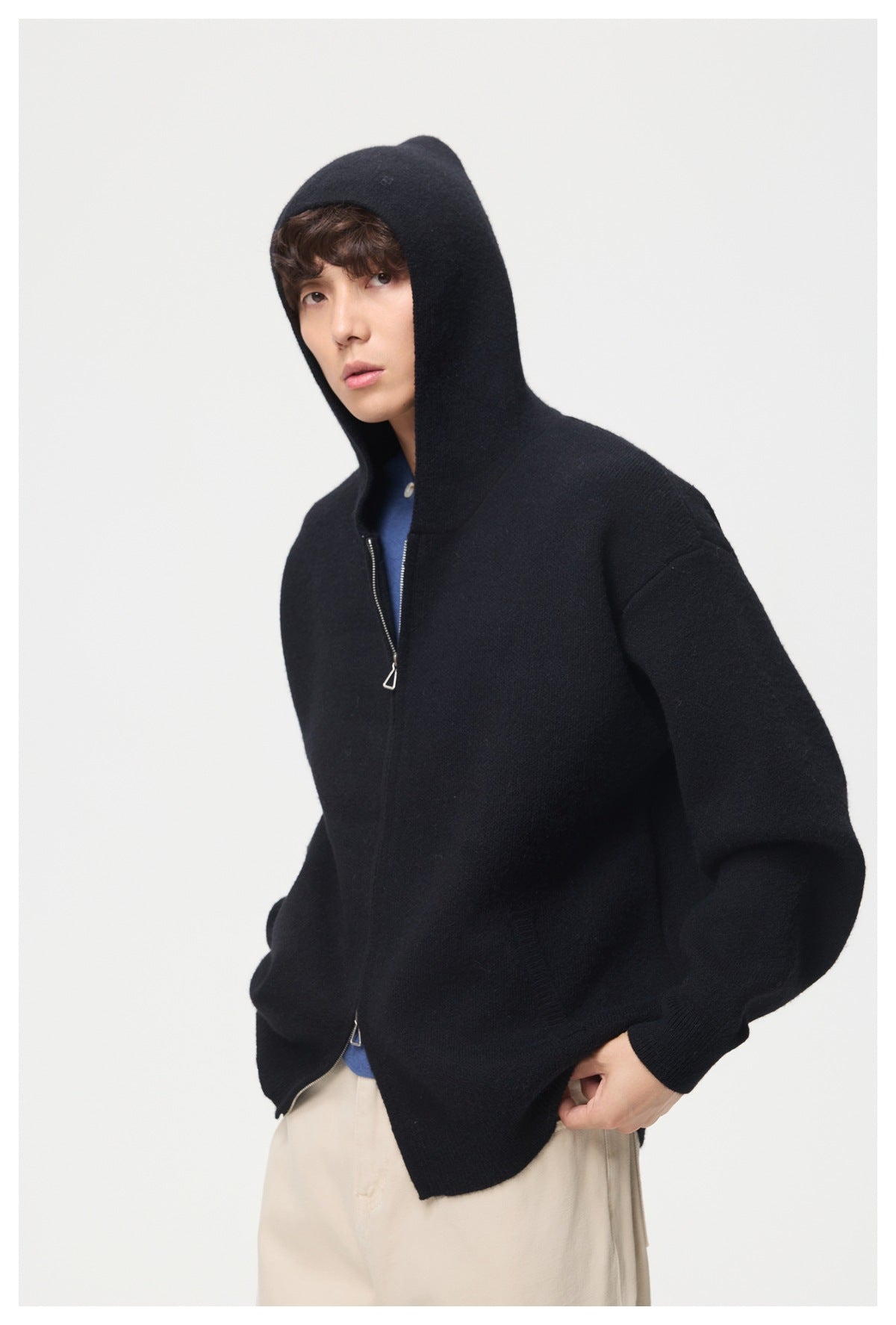 Model wearing a black zip-front hooded knit jacket with a high hood and roomy sleeves.